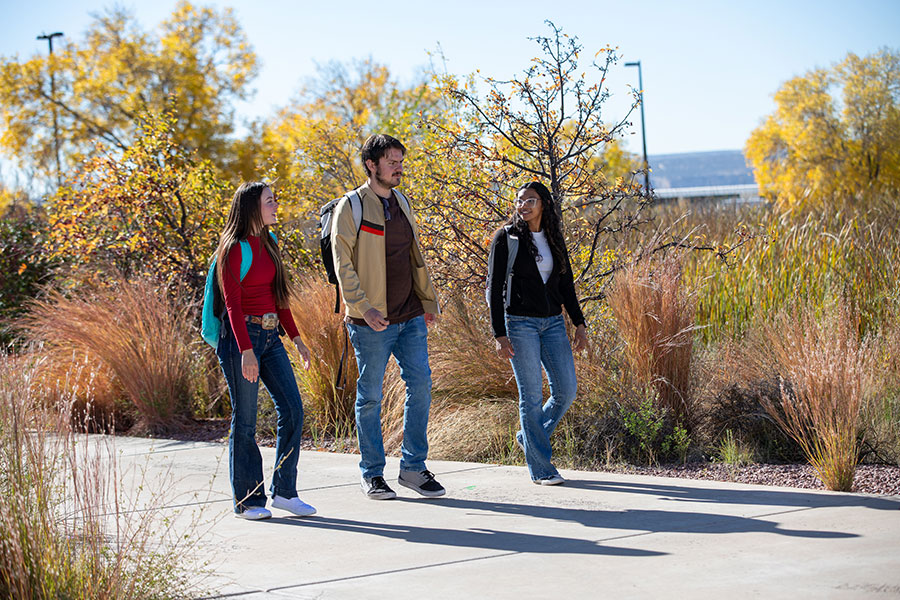 Three community college students walk together on campus discussing how to apply for financial aid, scholarships, and FAFSA options to help cover community college costs.