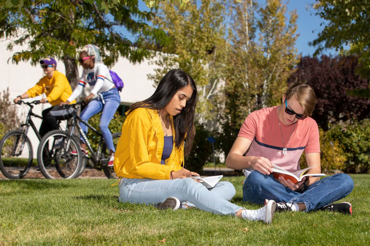 Group of San Juan College students sitting on the grass and two in the back riding bicycles