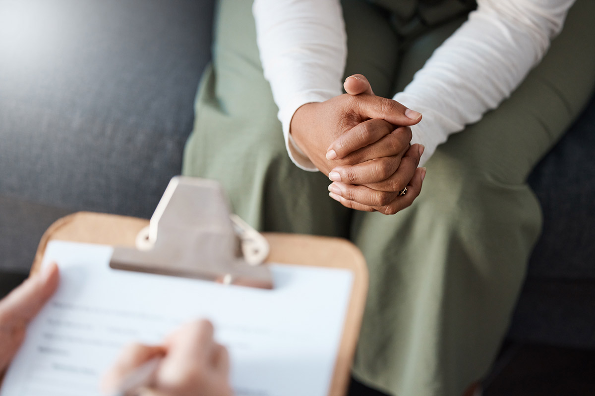 A doctor holding a clipboard speaking with an individual with there hands together