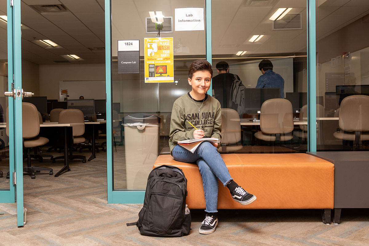 SJC student sitting on a bench outside of a classroom studying