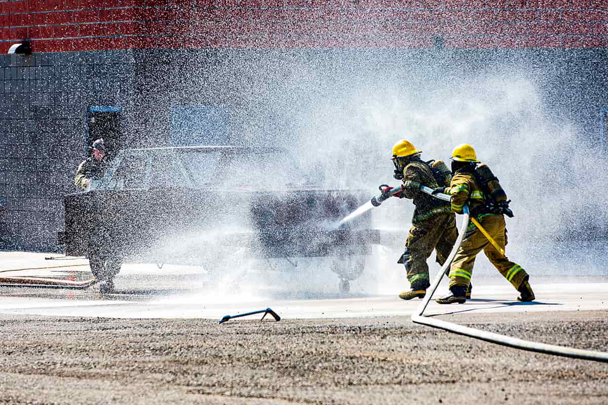 Two firemen practices putting out a vehicle fire at the fire science practice tower.