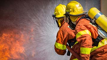 Two firemen spraying water on a fire.