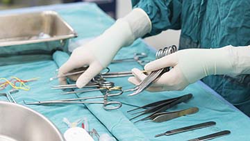 Hands with surgical gloves, handling surgical tools.