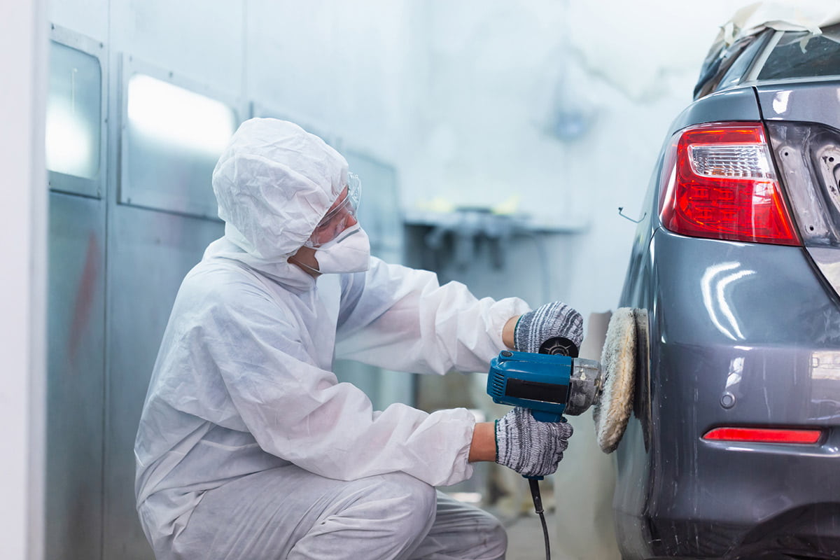 San Juan College student standing in front of a car frame in the auto body shop