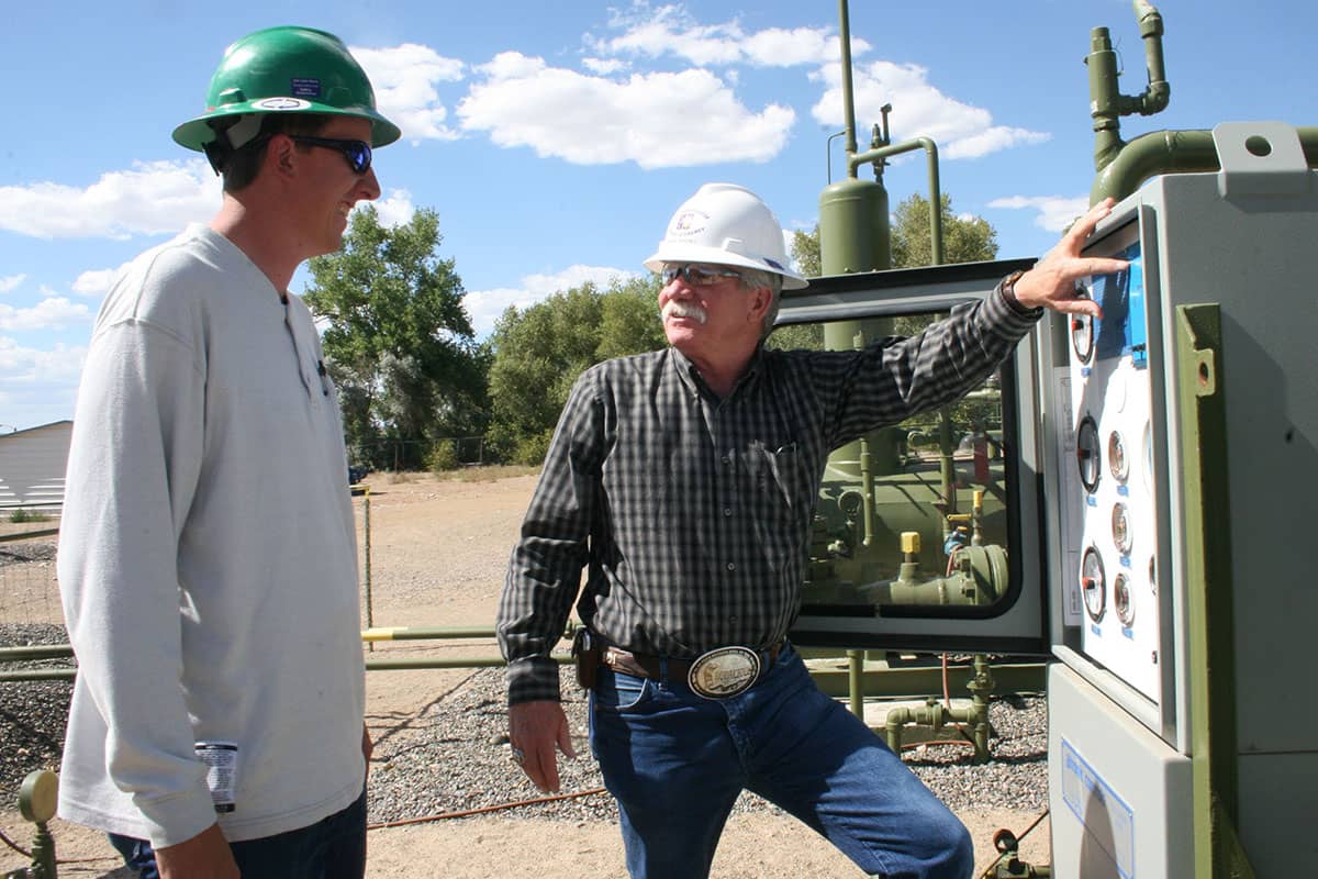 Two individuals in hard hats look at each other while standing next to a natural gas meter