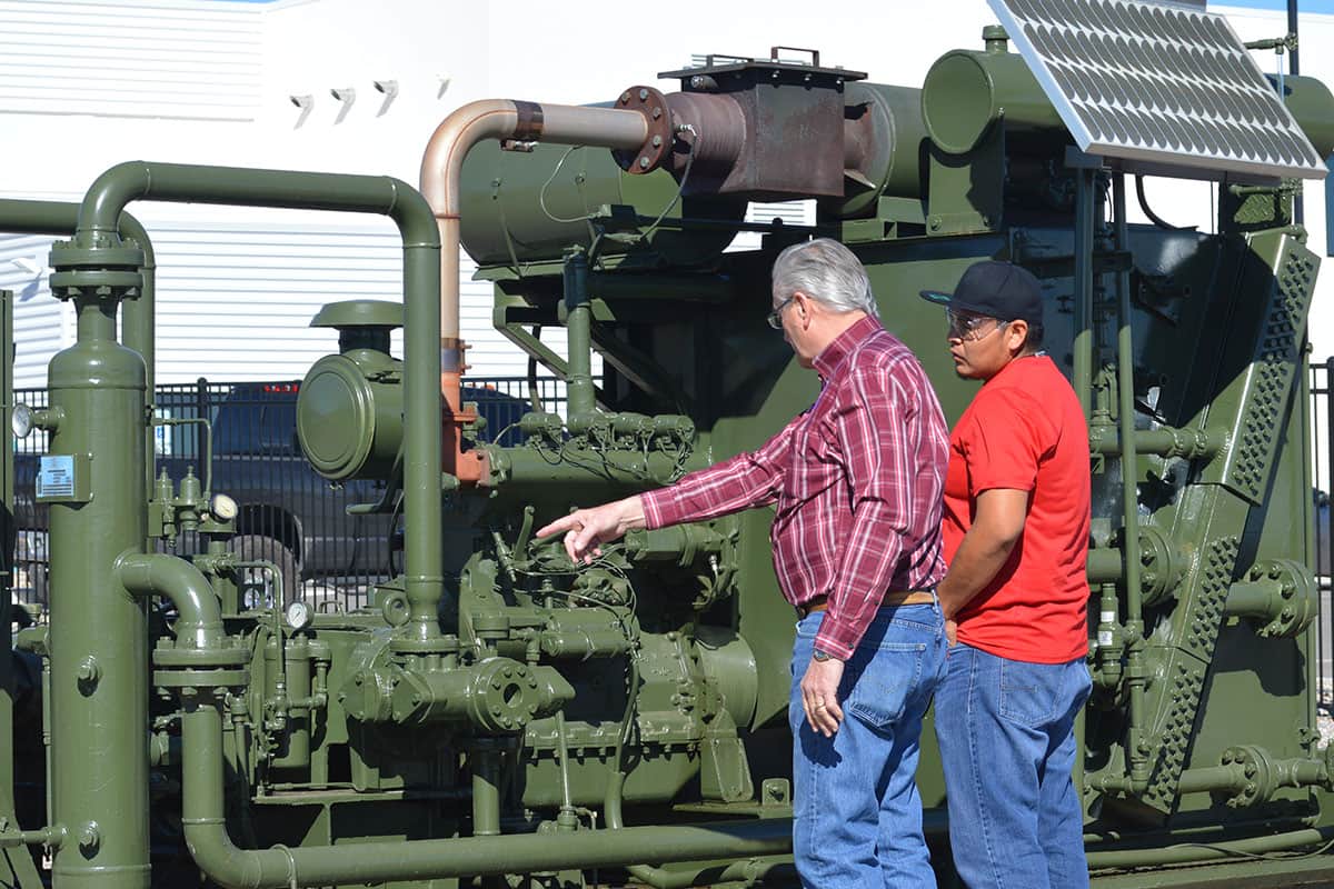 Two individuals look and point at natural gas valves in an outdoor setting