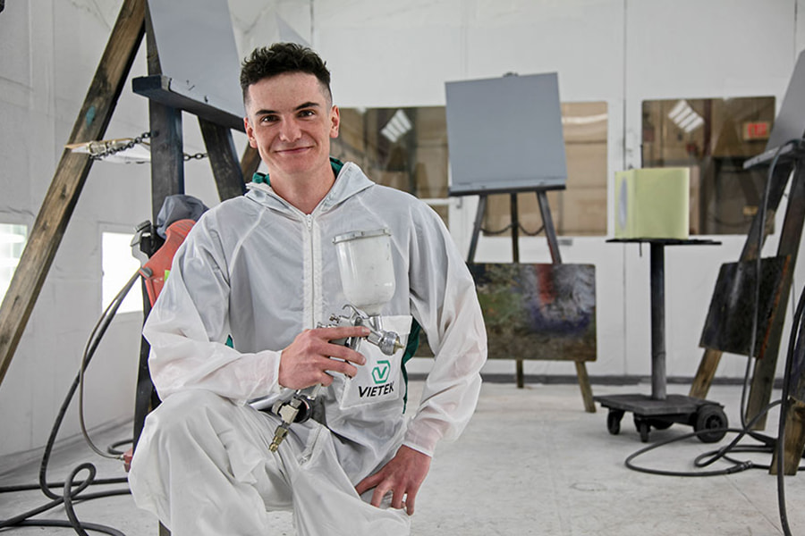 San Juan College student holding a paint sprayer in the auto body paint booth