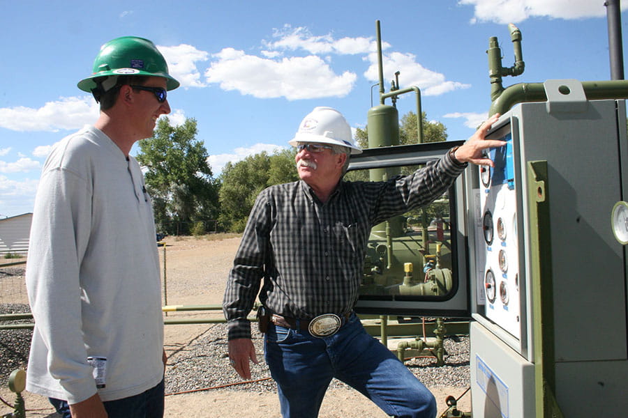 Two individuals in hard hats look at each other while standing next to a natural gas meter