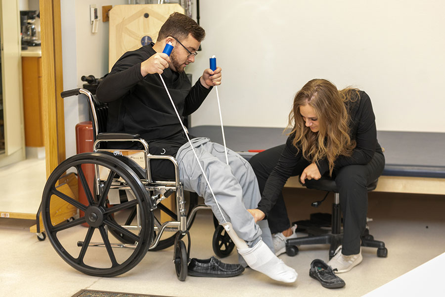 A student assesses the leg of another student who is sitting in a wheelchair