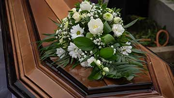 A brown wooden casket with white roses and greenery on top