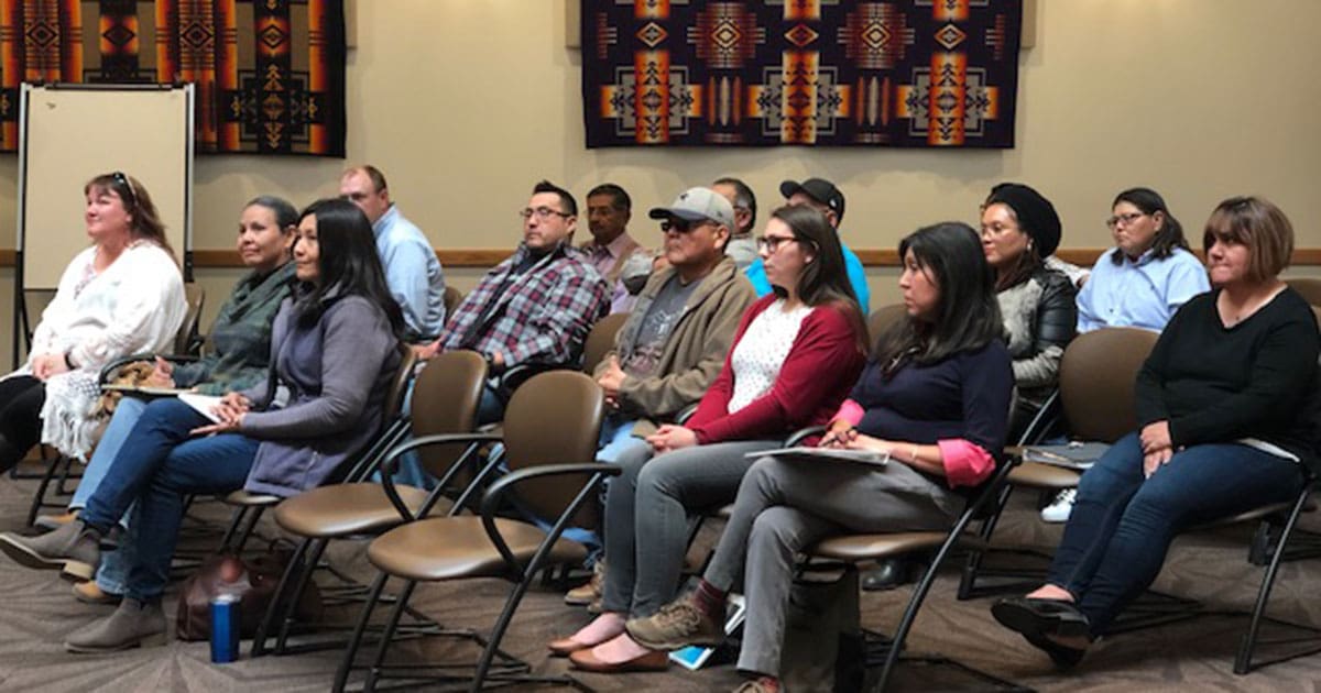 Group of people sit in rows, listening to a speaker.