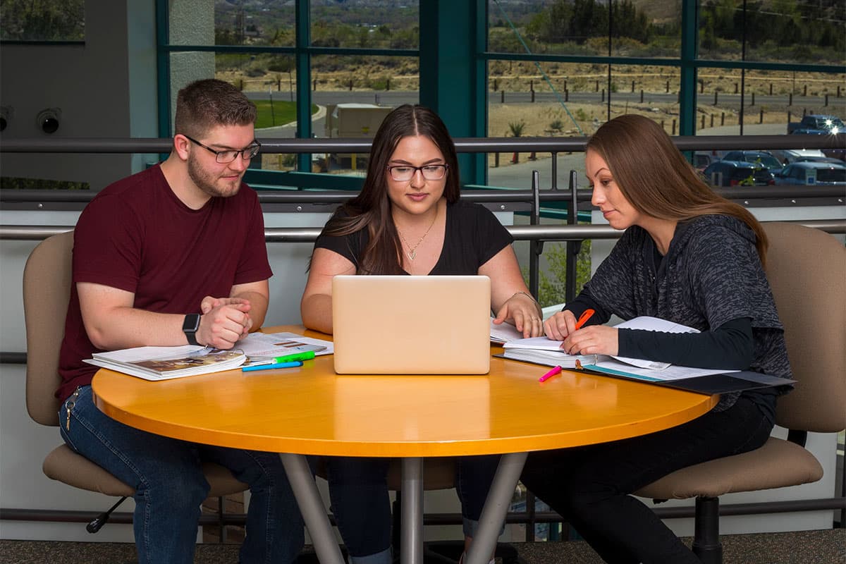 Three students at a table with one laptop