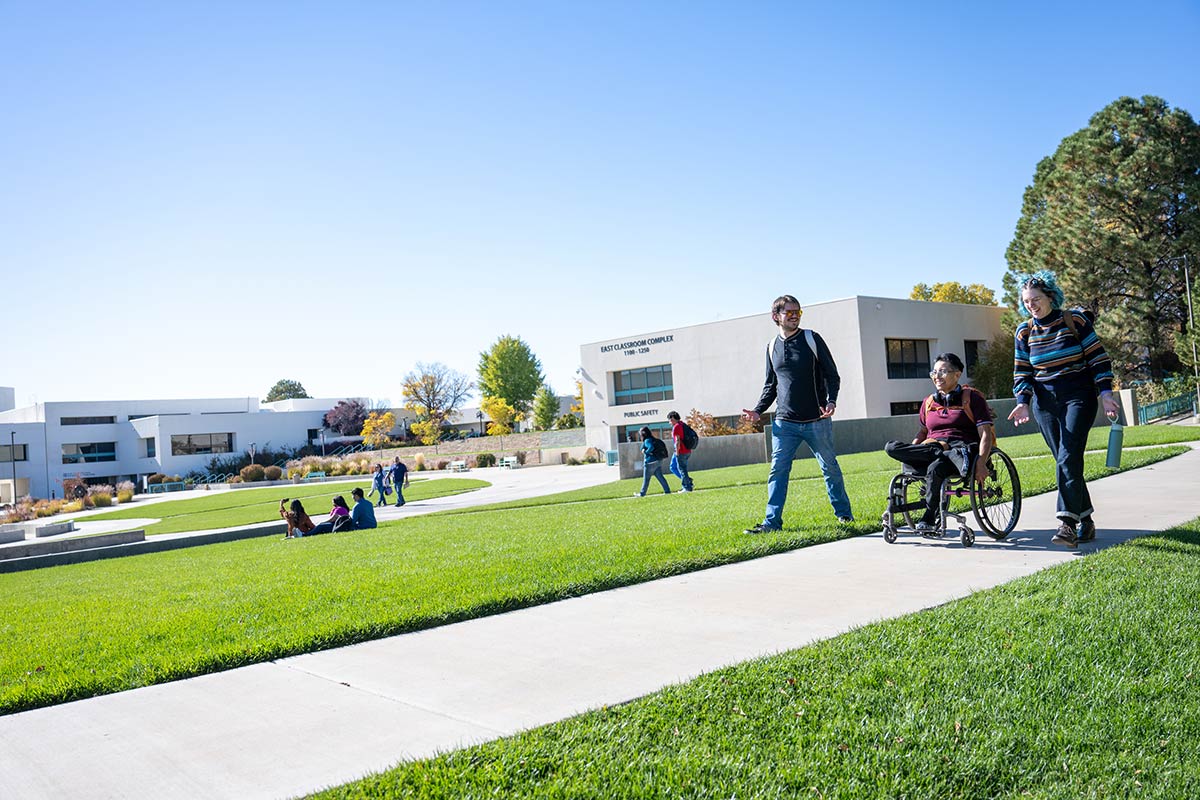 San Juan College students on campus. One student in a wheelchair smiling and talking with the other students.